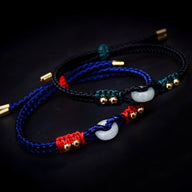 Bracelets en corde tressée noire, rouge et bleue avec pierres de jade blanches et détails dorés.