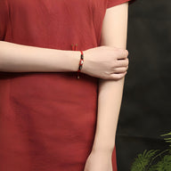 Bracelet tressé noir et rouge avec perles de jade, style mixte, porté au poignet.