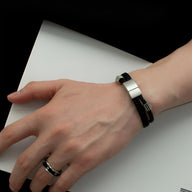 Bracelet en corde tressée noire à double tour avec fermoir argenté sur poignet masculin.