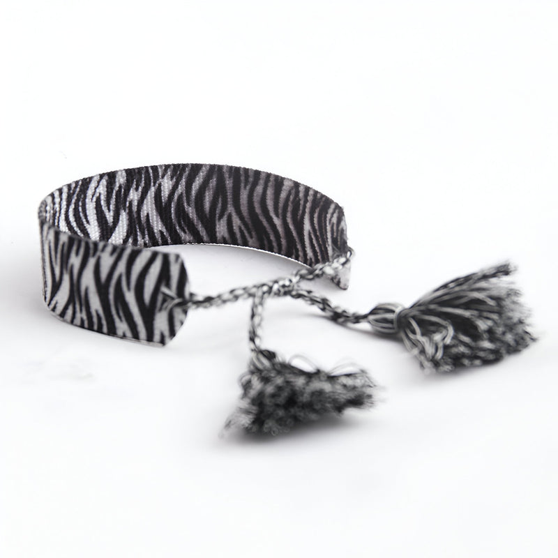 Bracelet en corde tressée à motif zèbre noir et blanc avec pompons assortis.