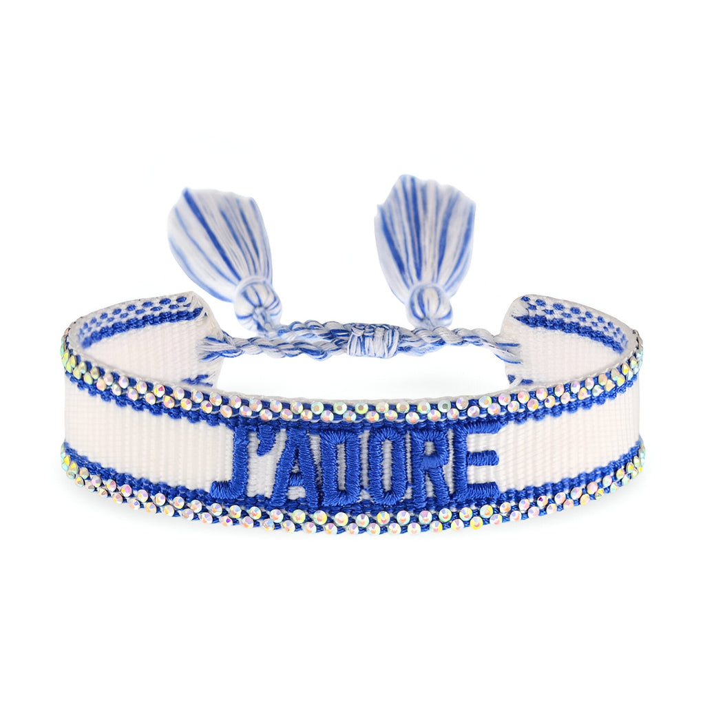 Bracelet en corde blanche et bleue tressée avec inscription "J'ADORE" en bleu et fermoir ajustable à pompons bleus.