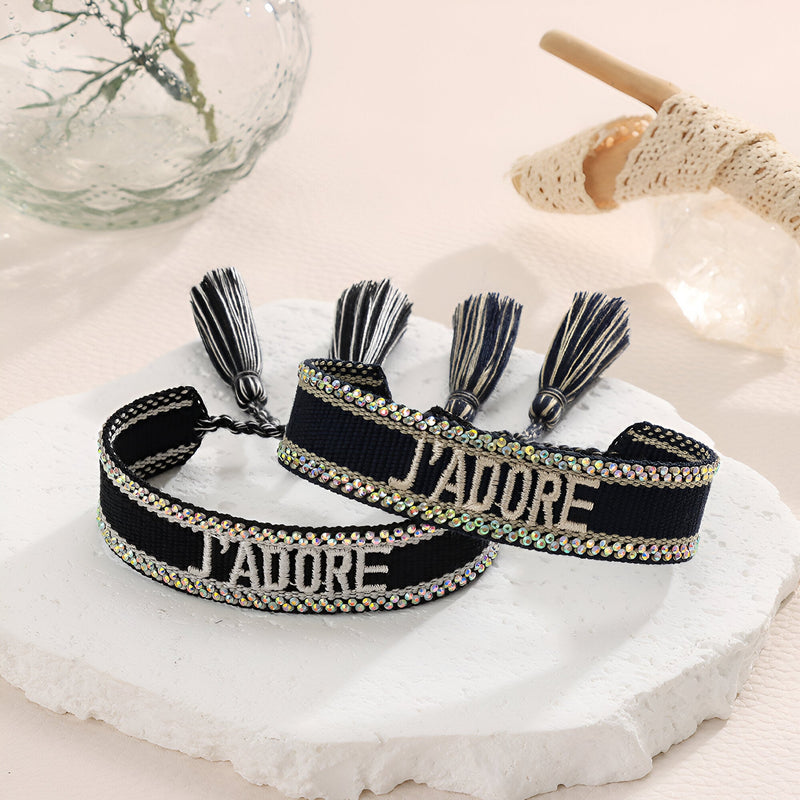 Bracelet en corde noire tressée avec pompons et inscription métallique « J'adore » et « J’adore ».