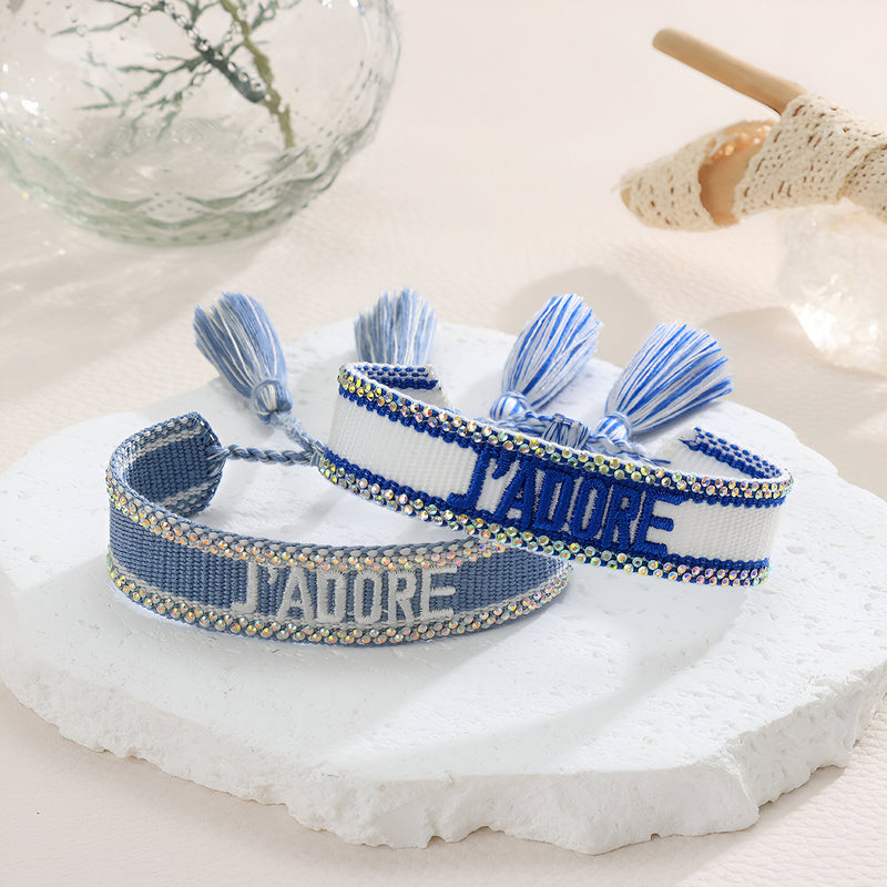 Bracelet en corde tressée bleu et blanc avec inscription "J'adore" et pompons assortis.