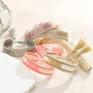 Bracelet en corde tressée beige avec inscription dorée "J'adore" et pompons assortis.