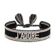 Bracelet en corde tressée noire avec inscription "J'ADORE" et bordure de strass scintillants, fermoir à nouer avec pompons.