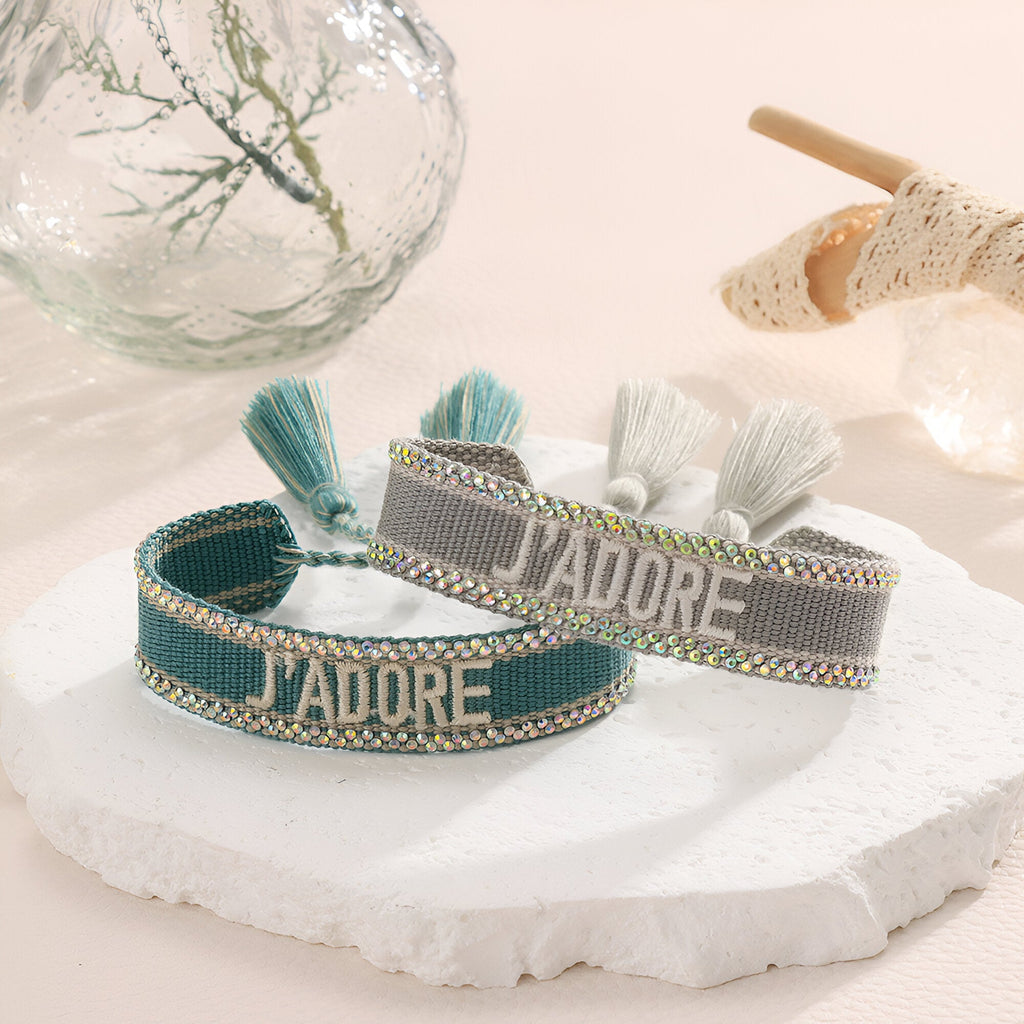 Bracelet en corde tressée bleu et gris avec inscription "J'adore" et pompons assortis.