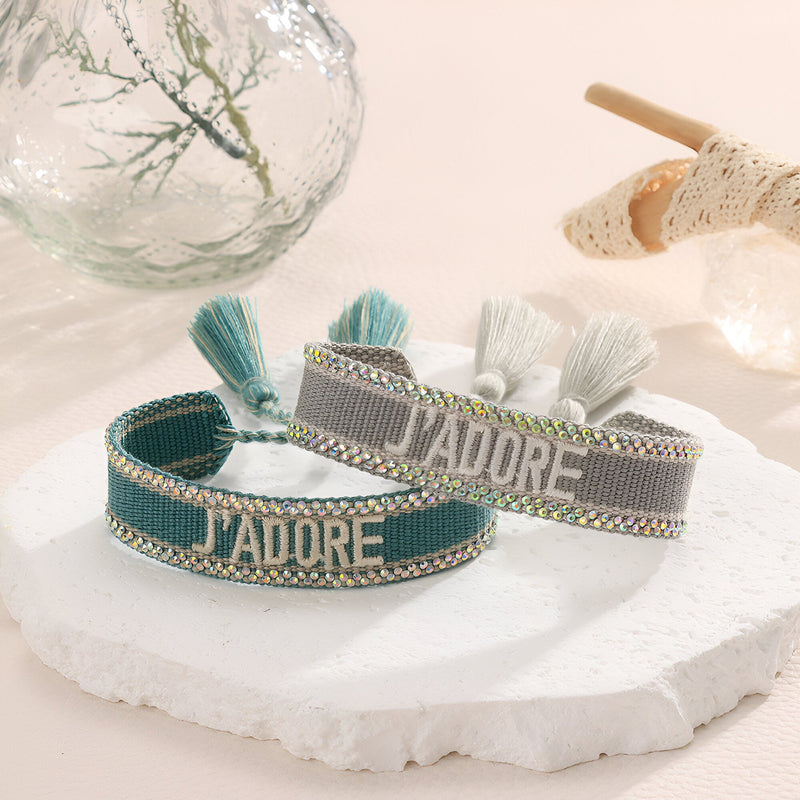Bracelet en corde tressée bleu et gris avec inscription "J'adore" et pompons assortis.