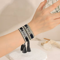 Bracelet en corde tressée noir et blanc avec inscription "J'adore" et pompons noirs.
