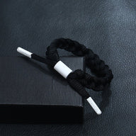 Bracelet en corde noire tressée avec embouts métalliques argentés sur fond noir mat.