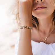 Bracelet en cristal multicolore avec petits papillons sur chaîne dorée, porté au poignet féminin.