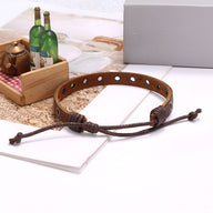 Bracelet en cuir marron avec anneaux métalliques incrustés et fermeture ajustable par cordon.
