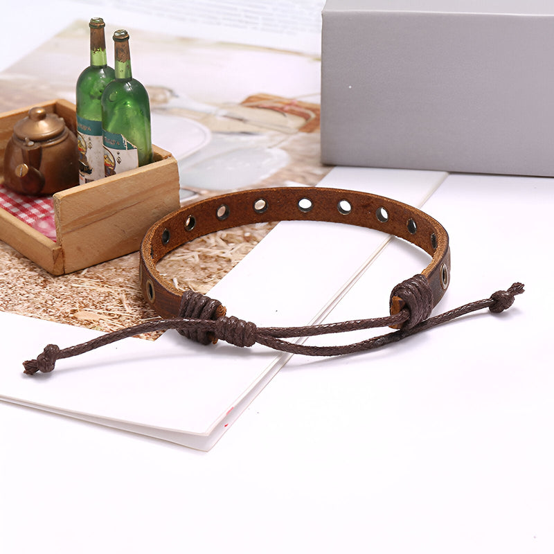 Bracelet en cuir marron avec anneaux métalliques incrustés et fermeture ajustable par cordon.