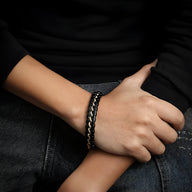 Bracelet en cuir noir avec détails ondulés et fermoir argenté porté au poignet.