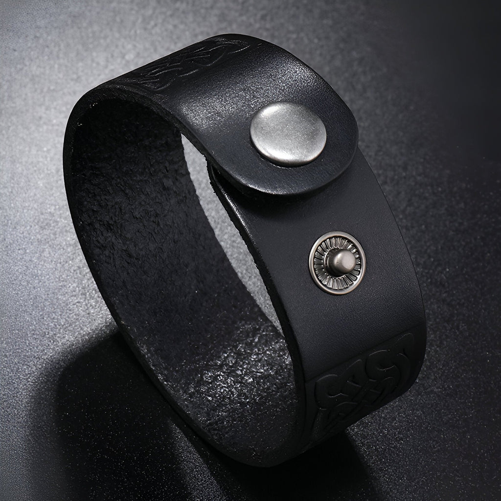 Bracelet en cuir noir avec motifs gaufrés et fermeture bouton-pression en métal argenté.
