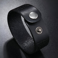 Bracelet en cuir noir avec motifs gaufrés et fermeture bouton-pression en métal argenté.