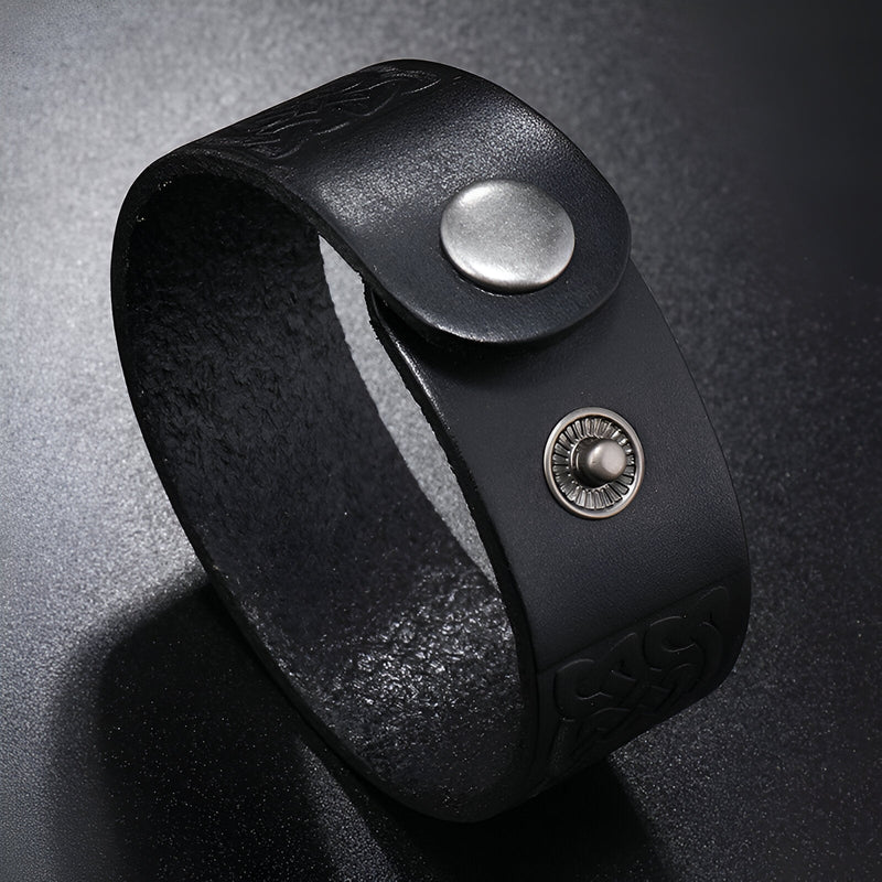 Bracelet en cuir noir avec motifs gaufrés et fermeture bouton-pression en métal argenté.