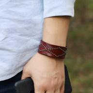 Bracelet en cuir café clouté style western avec motifs croisés portés au poignet masculin.