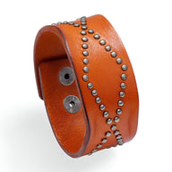 Bracelet large en cuir orange clouté de petits rivets métalliques formant un motif croisé vintage.