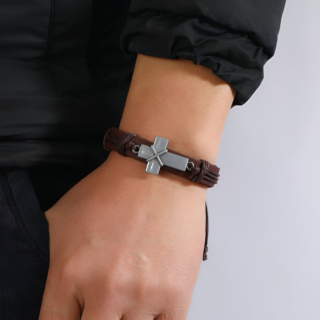 Bracelet en cuir marron tressé avec croix chrétienne en métal gris robuste pour homme.
