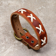 Bracelet en cuir marron avec croix tressées blanches et fermeture boucle métallique antique.