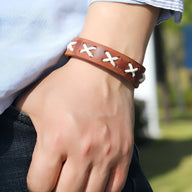 Bracelet en cuir marron pour homme avec croix tressées blanches, style masculin contemporain.