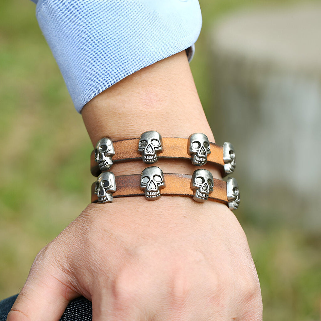 Bracelet en cuir marron double tour avec têtes de mort en métal argenté sur poignet masculin.