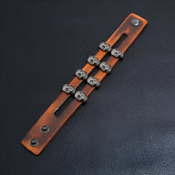 Bracelet en cuir marron double tour avec six têtes de mort en métal argenté et fermeture pression.