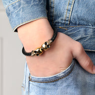 Bracelet en cuir noir avec deux têtes de mort dorées, style edgy et masculin.