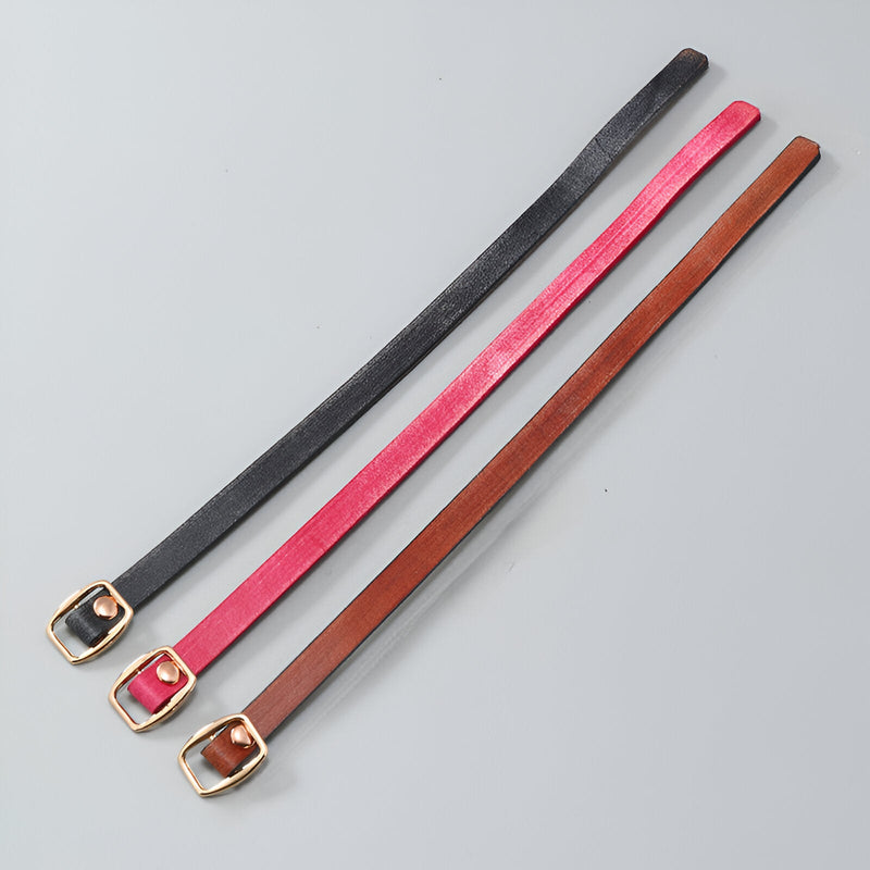 Trois bracelets en cuir fins pour femme, couleurs marron, rose vif et noir, boucles dorées élégantes.