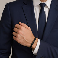 Bracelet en cuir noir avec détails métalliques argentés, porté avec un costume bleu marine et une cravate noire.