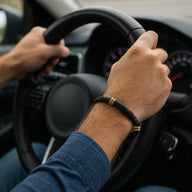 Bracelet en cuir noir tressé avec détails métalliques dorés porté au poignet d’un homme au volant.