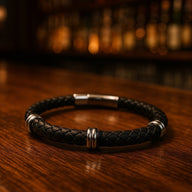 Bracelet en cuir tressé noir avec détails métalliques argentés et fermoir en acier inoxydable.