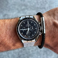 Bracelet en cuir noir tressé avec fermoir en acier inoxydable argenté, style alluré, porté au poignet.