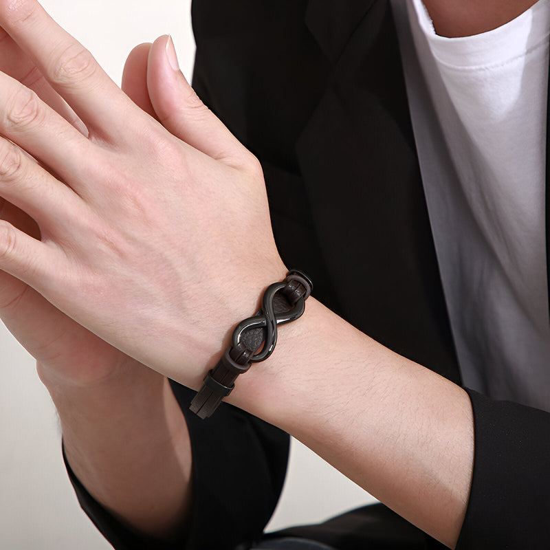 Bracelet noir en cuir avec motif infini en acier inoxydable porté au poignet masculin.