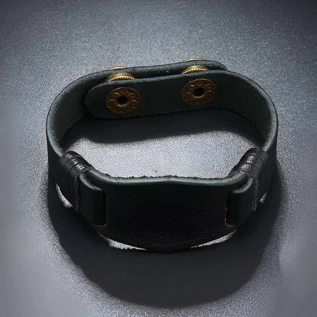 Bracelet large en cuir noir pour homme avec fermeture à boutons-pression dorés.