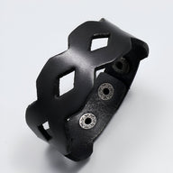 Bracelet large en cuir noir avec découpes géométriques, fermoir à boutons-pression métal.