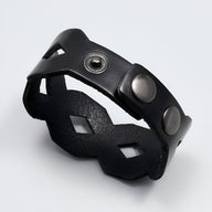 Bracelet large en cuir noir avec découpes géométriques et fermoir à boutons-pression en métal.