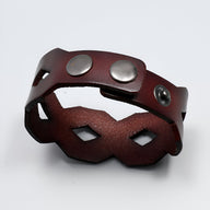 Bracelet large en cuir café avec formes géométriques et fermoir à boutons-pression métalliques.