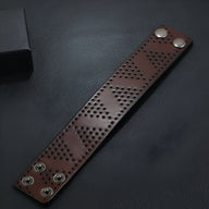 Bracelet large en cuir café avec motif de trous géométriques et fermoirs à pression métalliques.