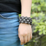 Bracelet manchette en cuir café orné de fleurs grises et blanches sur poignet féminin.