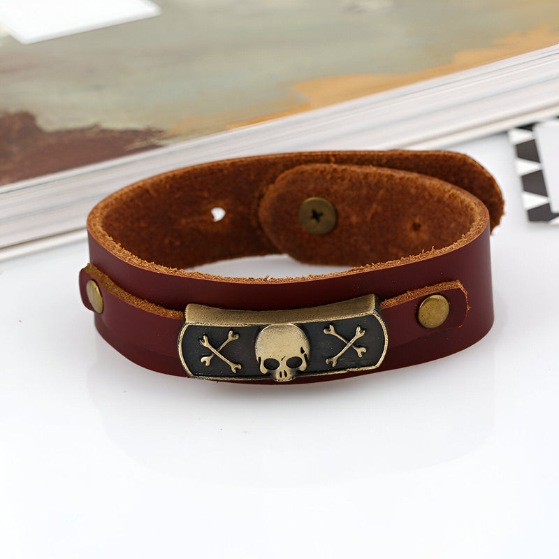 Bracelet en cuir marron avec motif tête de mort et os croisés en métal doré.