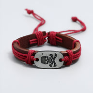 Bracelet en cuir marron avec cordons rouges et plaque métal tête de mort gravée.