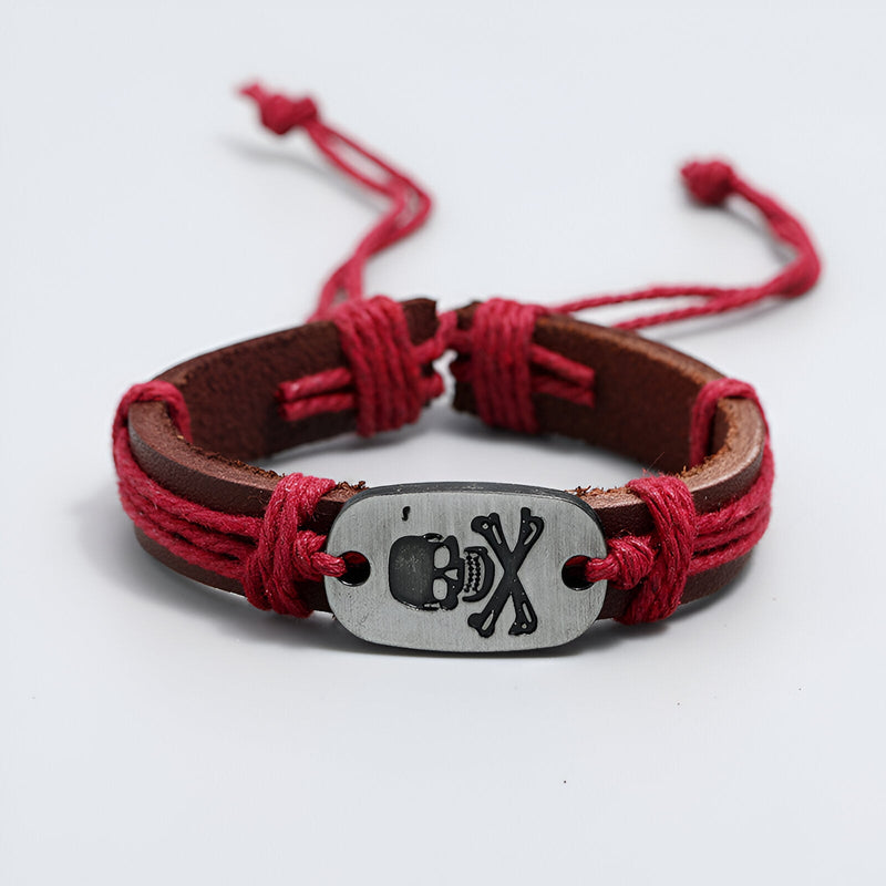 Bracelet en cuir marron avec cordons rouges et plaque métal tête de mort gravée.