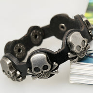 Bracelet en cuir noir avec têtes de mort en métal argenté et fermeture à pression.