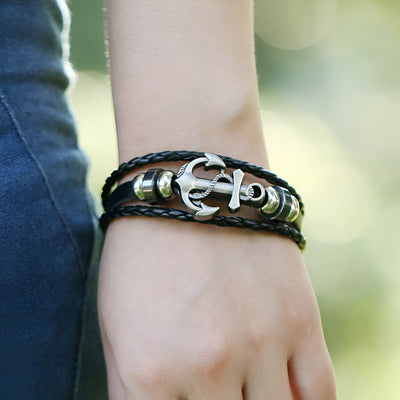 Bracelet en cuir marron multi-rangs avec ancre marine argentée et perles métalliques sur poignet.