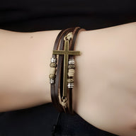Bracelet homme en cuir marron multi-rangs avec charm croix métal doré et perles décoratives.