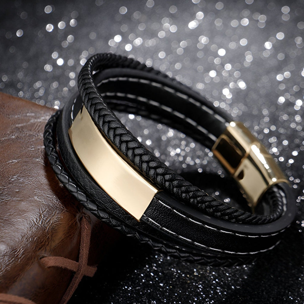 Bracelet multi-rangs en cuir noir avec plaque métallique dorée et fermoir magnétique doré.
