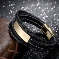 Bracelet multi-rangs en cuir noir avec plaque métallique dorée et fermoir magnétique doré.