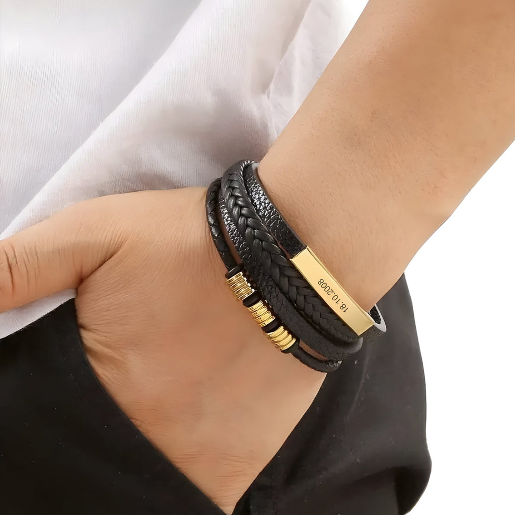 Bracelet multi-rangs en cuir noir avec plaque métallique gravée dorée et petits anneaux dorés.