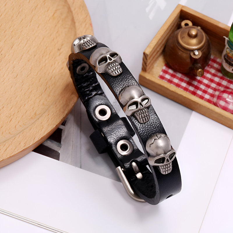 Bracelet en cuir noir avec plusieurs têtes de mort métalliques et boucle argentée.